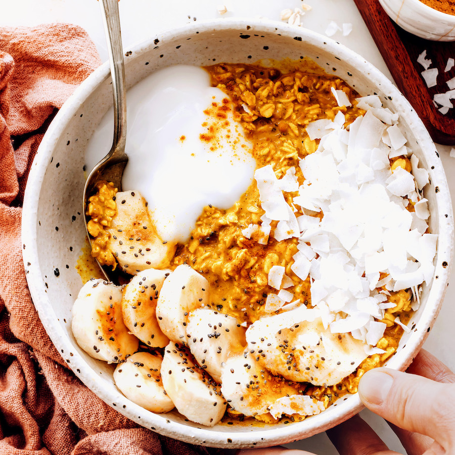 Bowl of golden milk overnight oats topped with banana, coconut yogurt, coconut flakes, and chia seeds