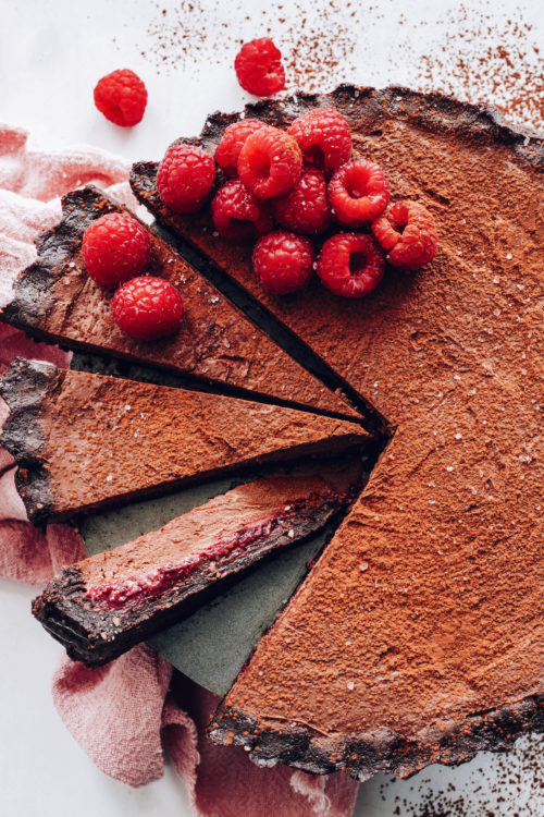 Partially sliced vegan chocolate ganache tart topped with fresh raspberries