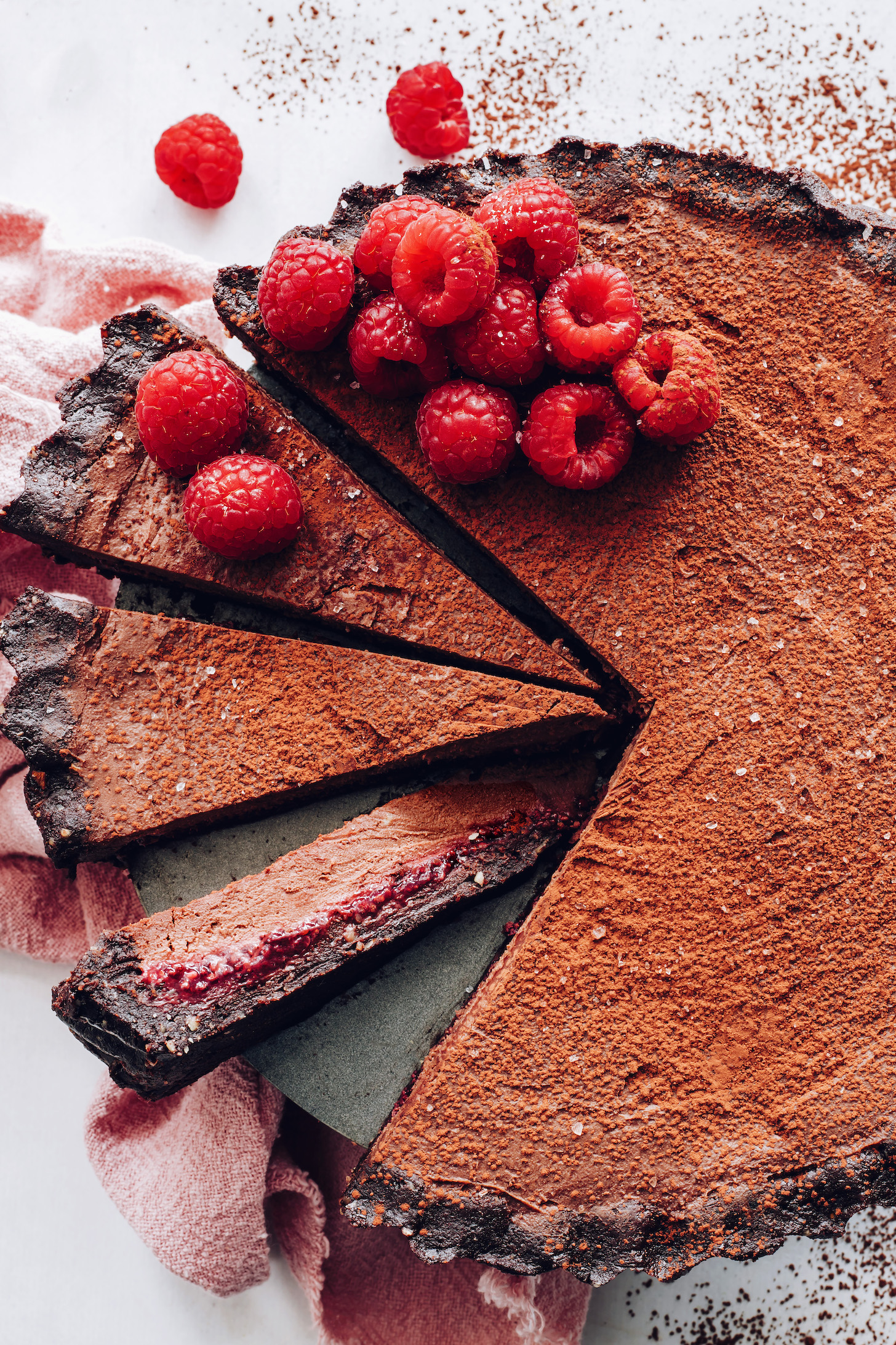 Vegan chocolate ganache tart topped with fresh raspberries and a dusting of cocoa powder