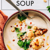 Bowl of vegan and gluten-free roasted cauliflower soup with pieces of roasted cauliflower, pine nuts, and cilantro