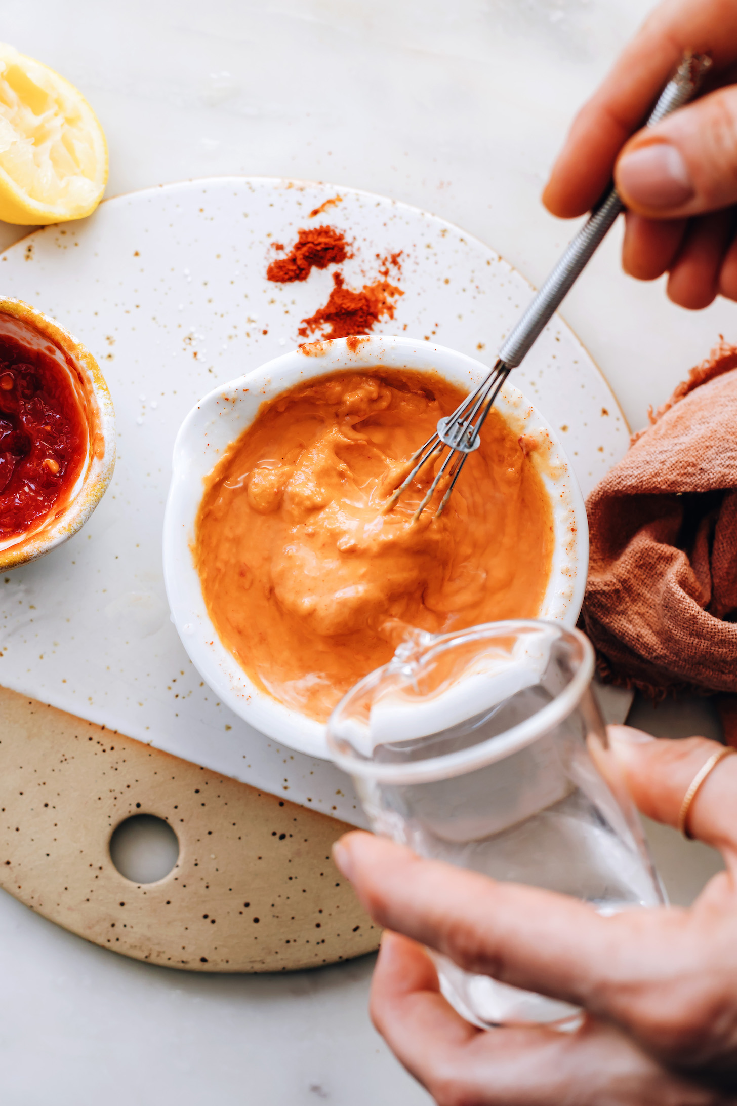 Pouring water into a bowl to thin the harissa tahini sauce
