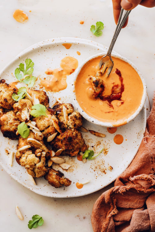 Dipping roasted cauliflower in a bowl of harissa tahini sauce