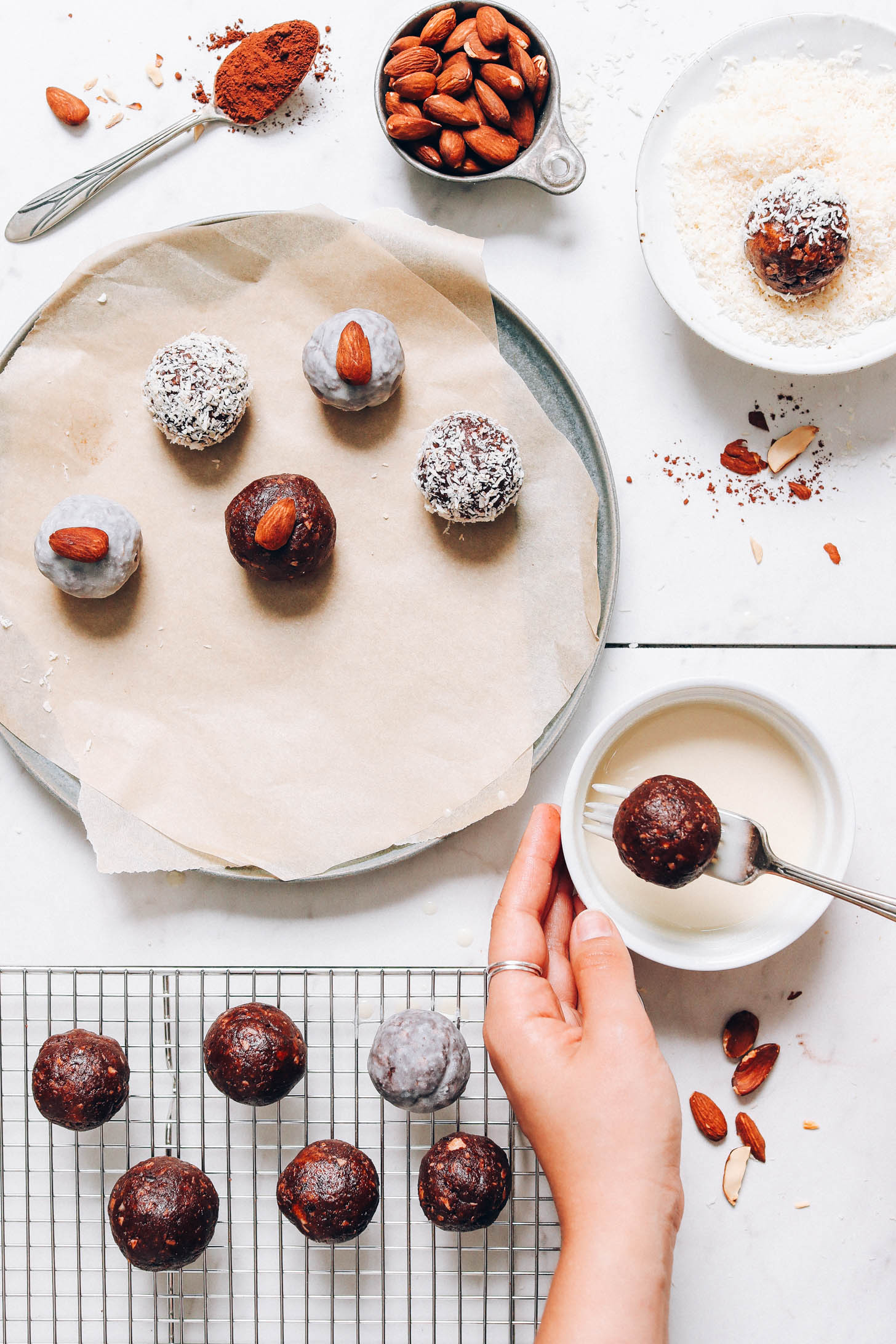 Dipping an Almond Joy Energy Bite in a bowl of glaze next to more energy bites
