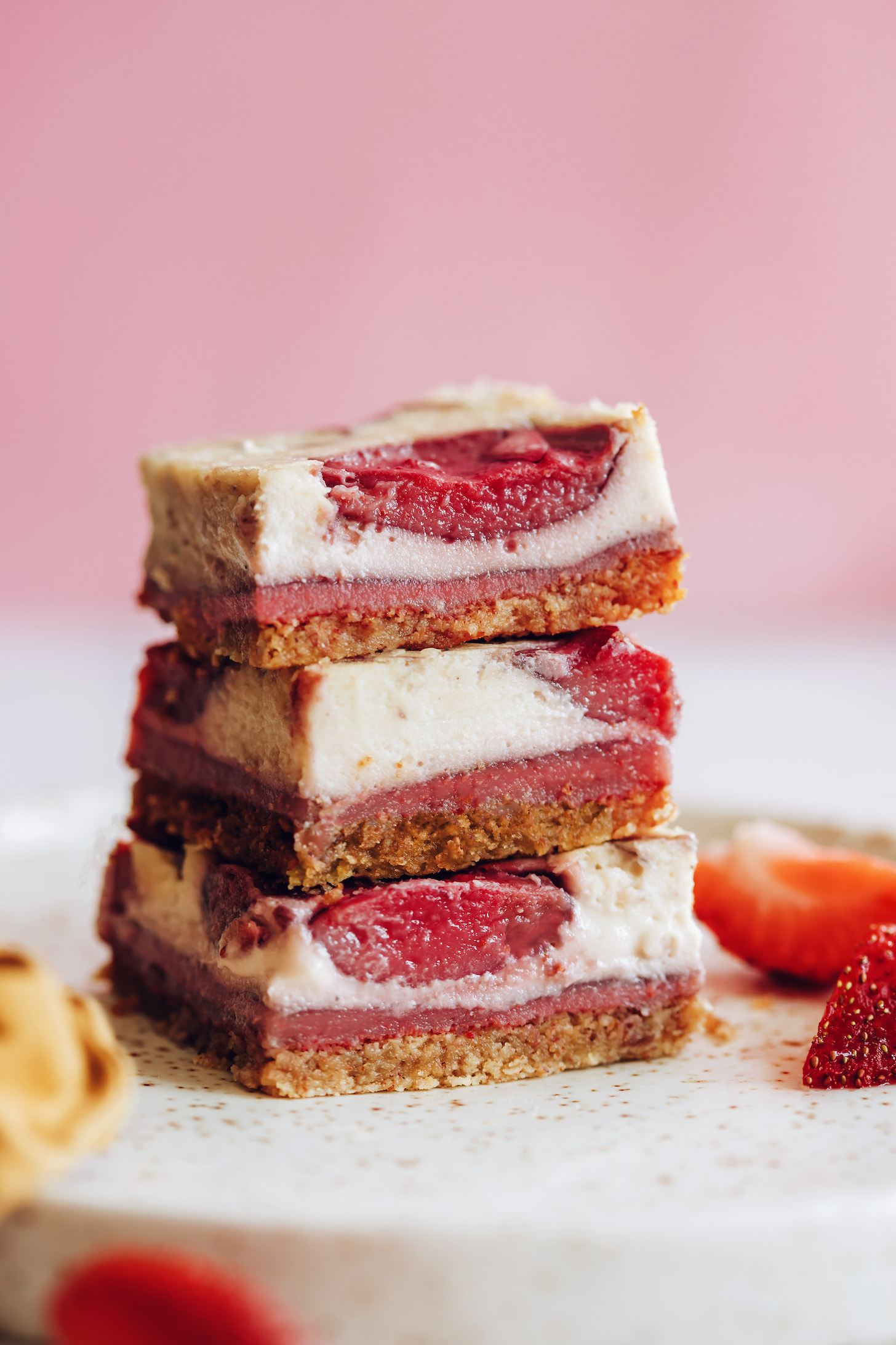Plate of strawberry cheesecake bars next to fresh strawberries