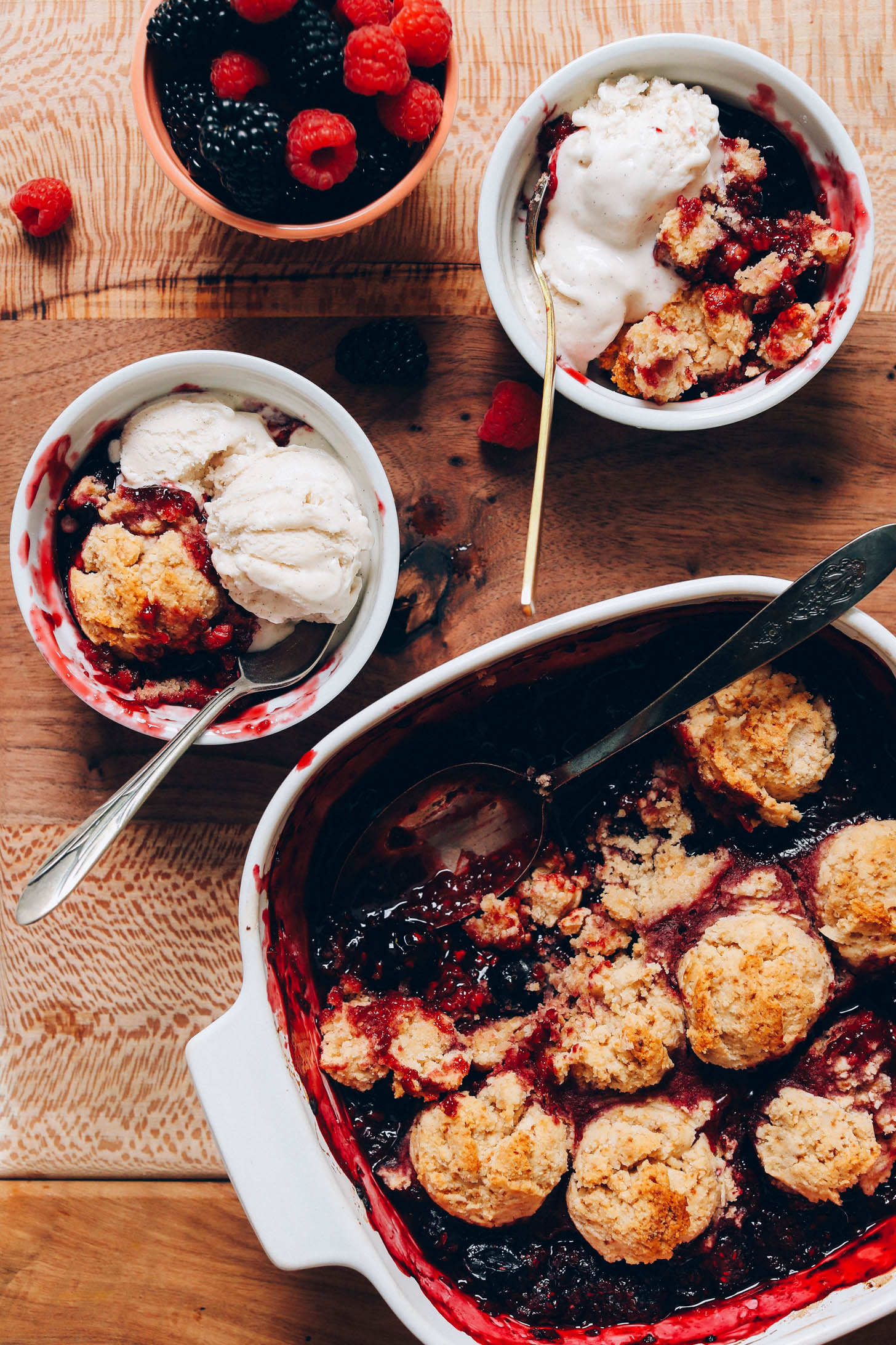 Pan of berry cobbler and two bowls of cobbler with scoops of vegan vanilla ice cream