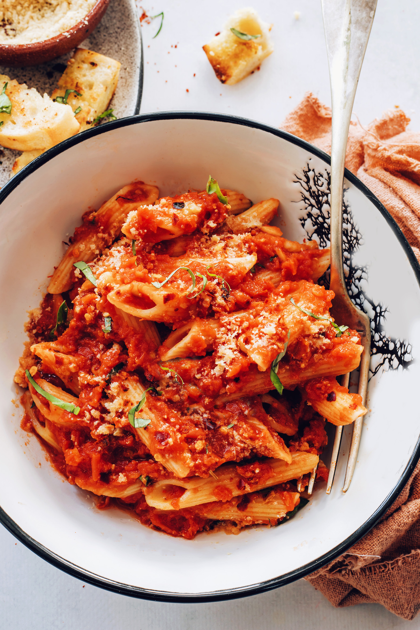 Bowl of penne arrabbiata topped with vegan parmesan cheese and fresh basil