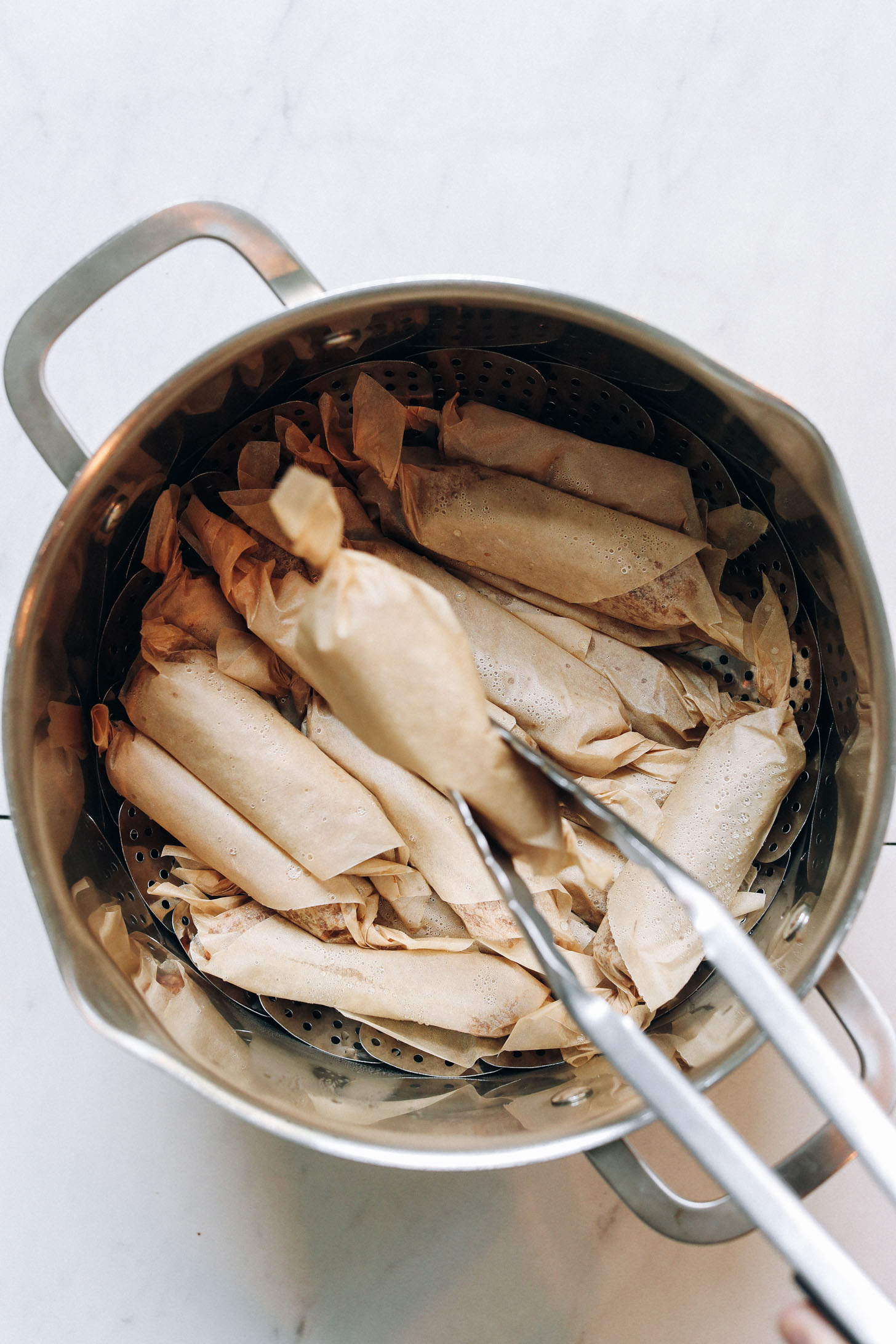 Using tongs to remove a vegan sausage link for a steaming pan