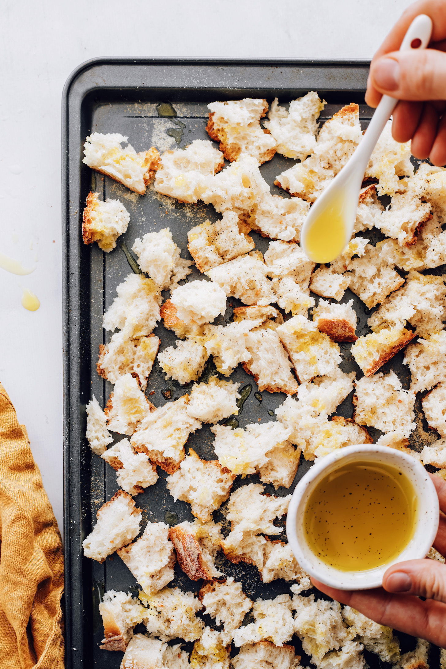 Drizzling olive oil over pieces of bread on a baking sheet