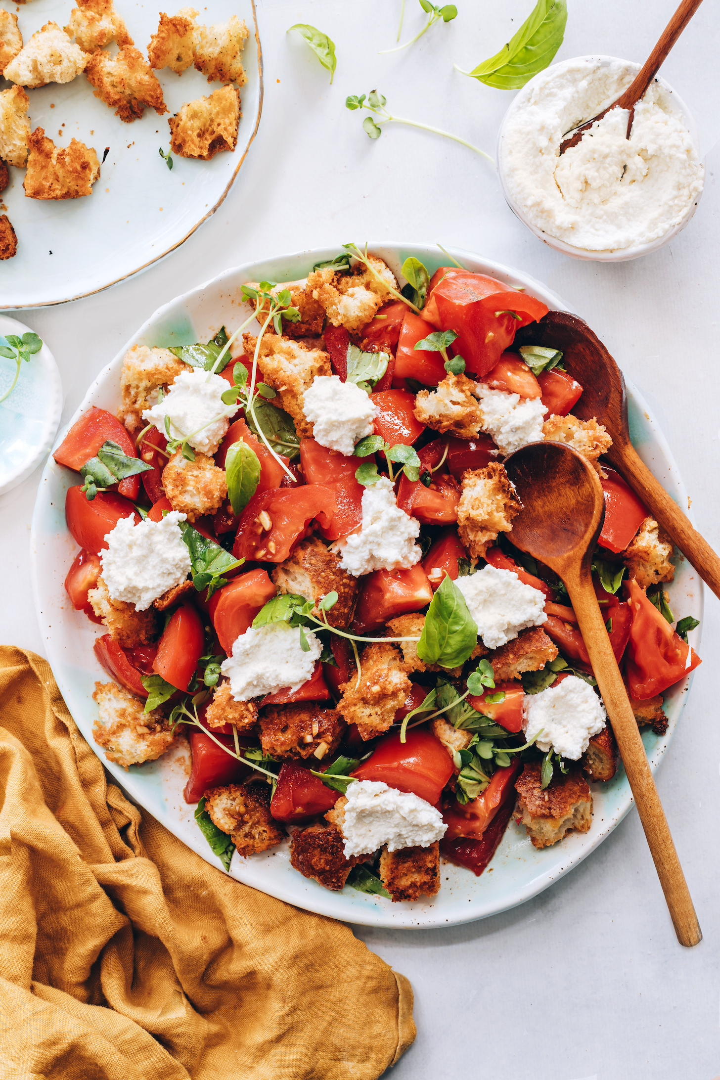 Platter of tomato panzanella salad with basil, microgreens, and cashew ricotta