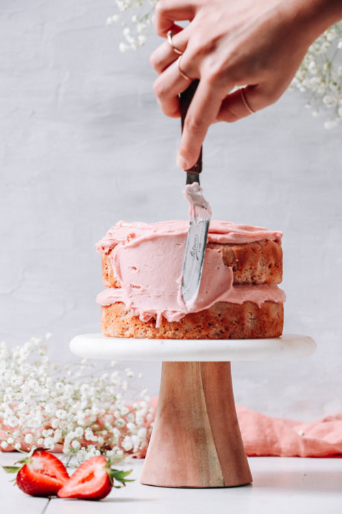 Spreading vegan strawberry frosting over a strawberry cake