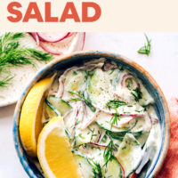 Bowl of vegan and gluten-free creamy cucumber salad with fresh lemon wedges, dill, and radishes on the side