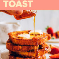 A plate of easy vegan french toast with vegan butter and strawberries, being drizzled with maple syrup