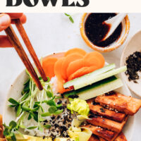 Using chopsticks to pick up a bite of rice and veggies from a vegan sushi bowl