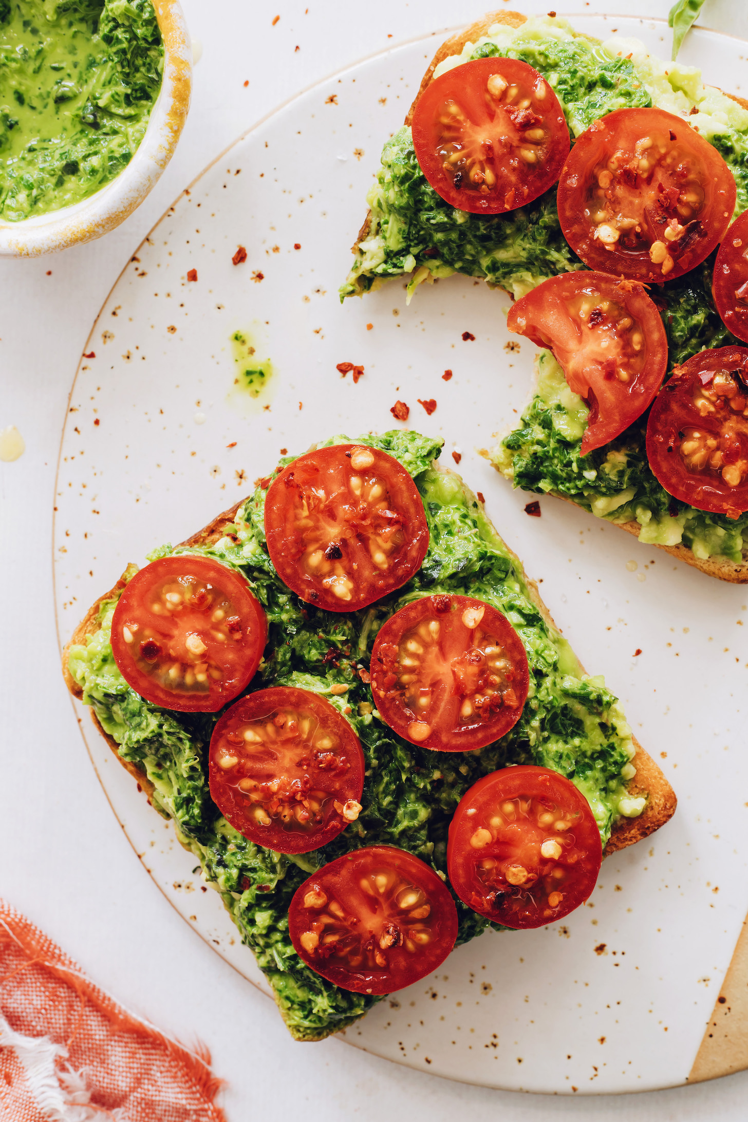 Two slices of pesto avocado toast topped with red pepper flakes