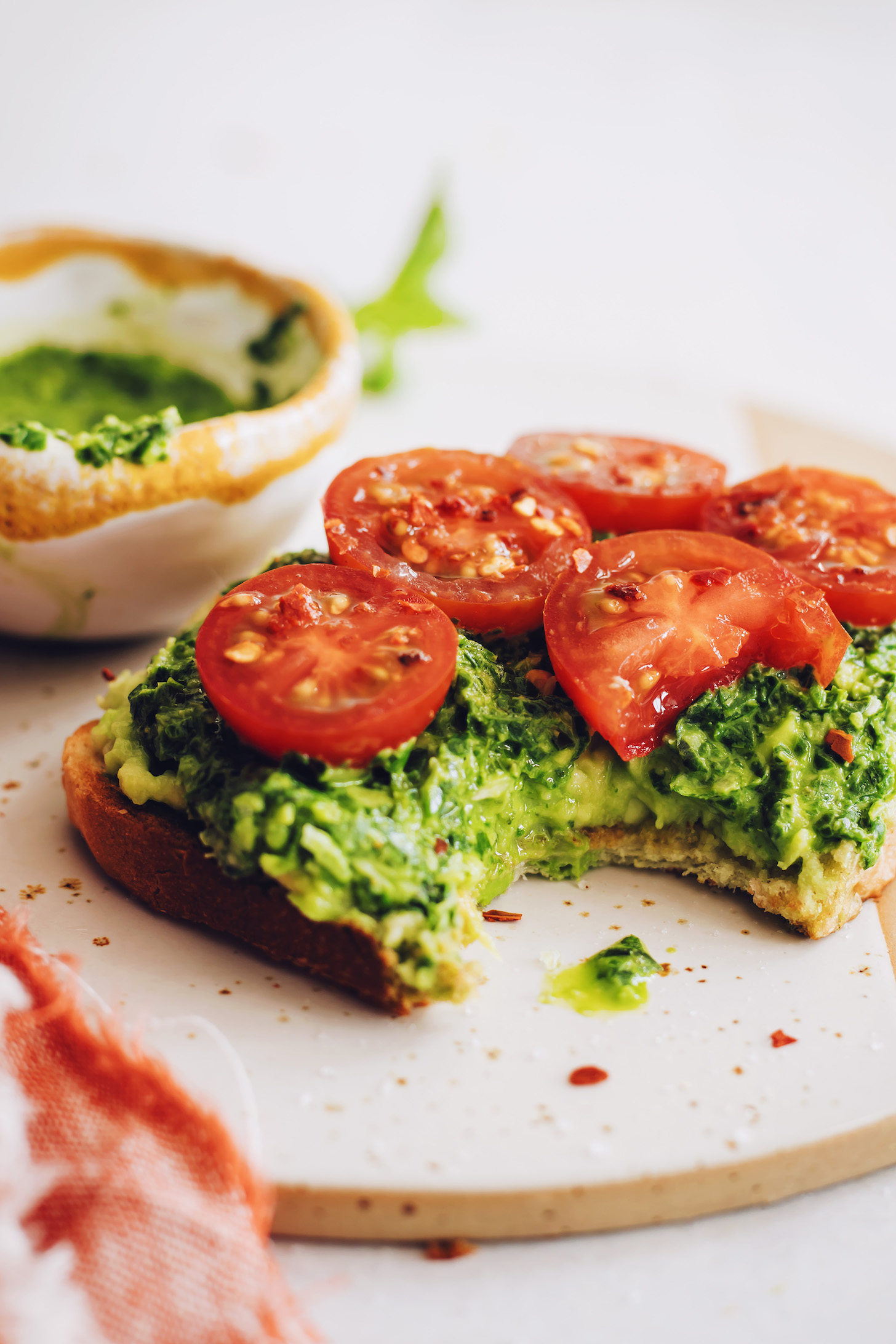 Bite eaten from a slice of pesto avocado toast with fresh tomatoes