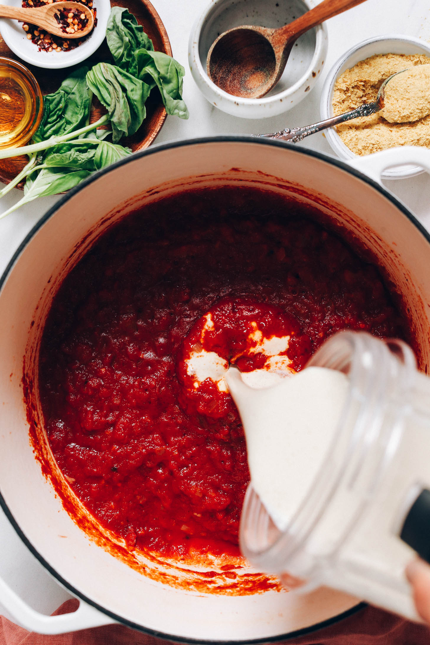Pouring cashew cream from a blender into a pan of tomato sauce