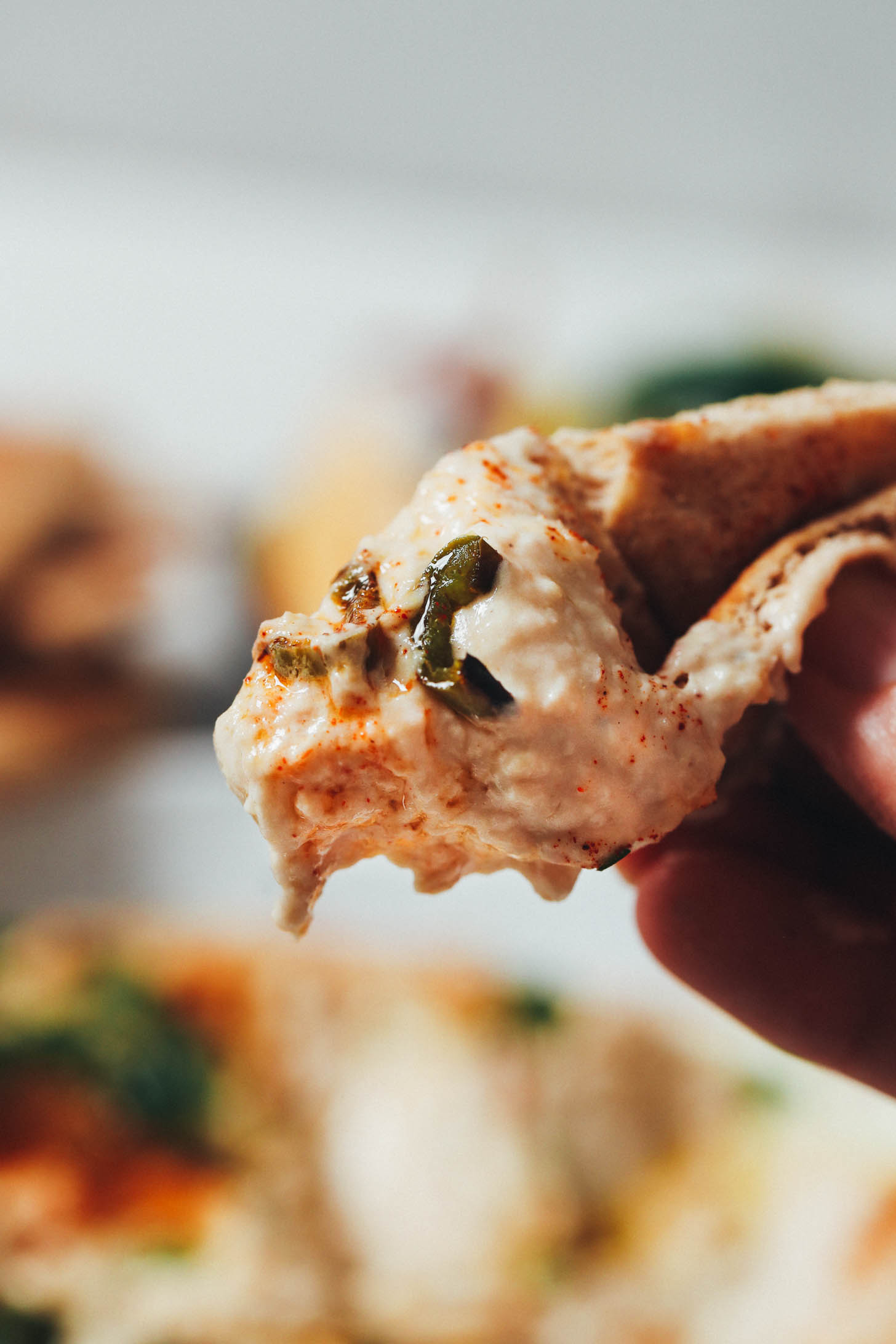 Holding a piece of pita bread dripping with white bean dip