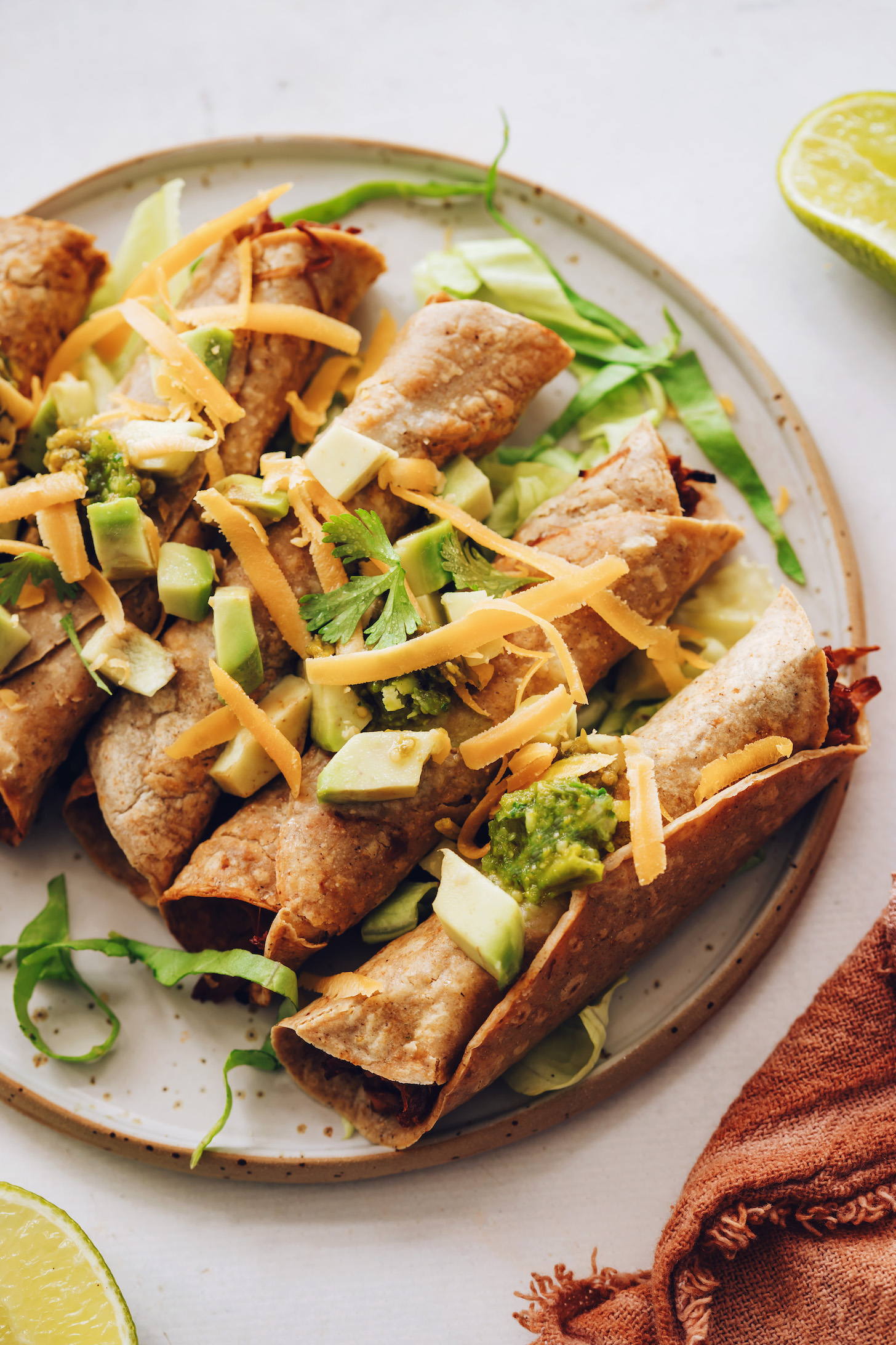 Plate of jackfruit taquitos with avocado, cilantro, lettuce, vegan cheddar, and tomatillo salsa