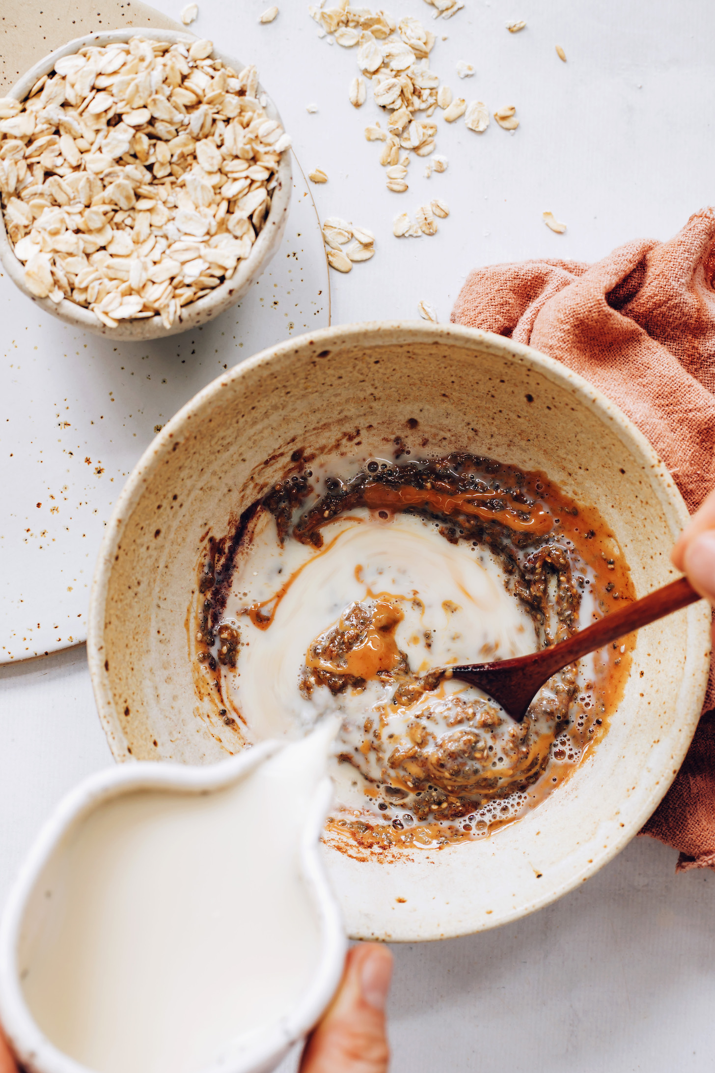 Pouring almond milk over chia seeds, maple syrup, cinnamon, almond butter, and vanilla