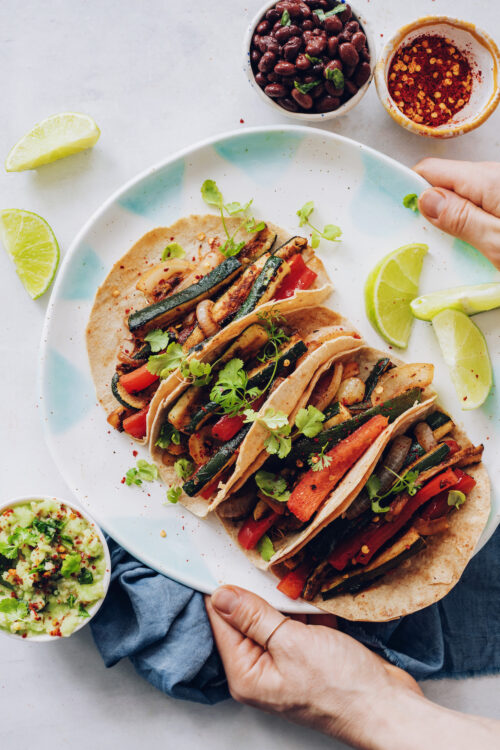 Hands holding a platter of vegan tacos with zucchini and bell pepper