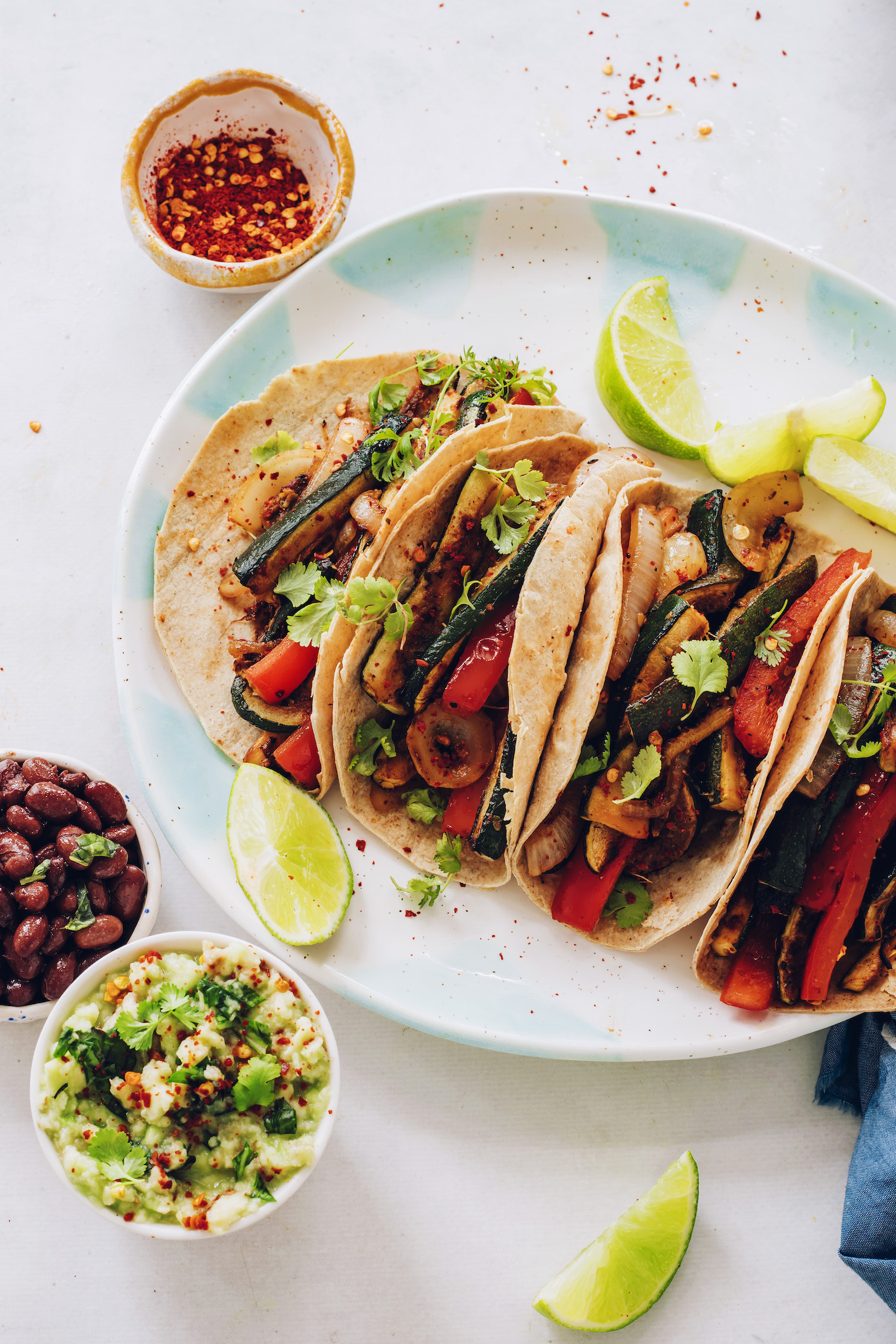 Guacamole, black beans, and red pepper flakes around a plate of bell pepper and zucchini tacos