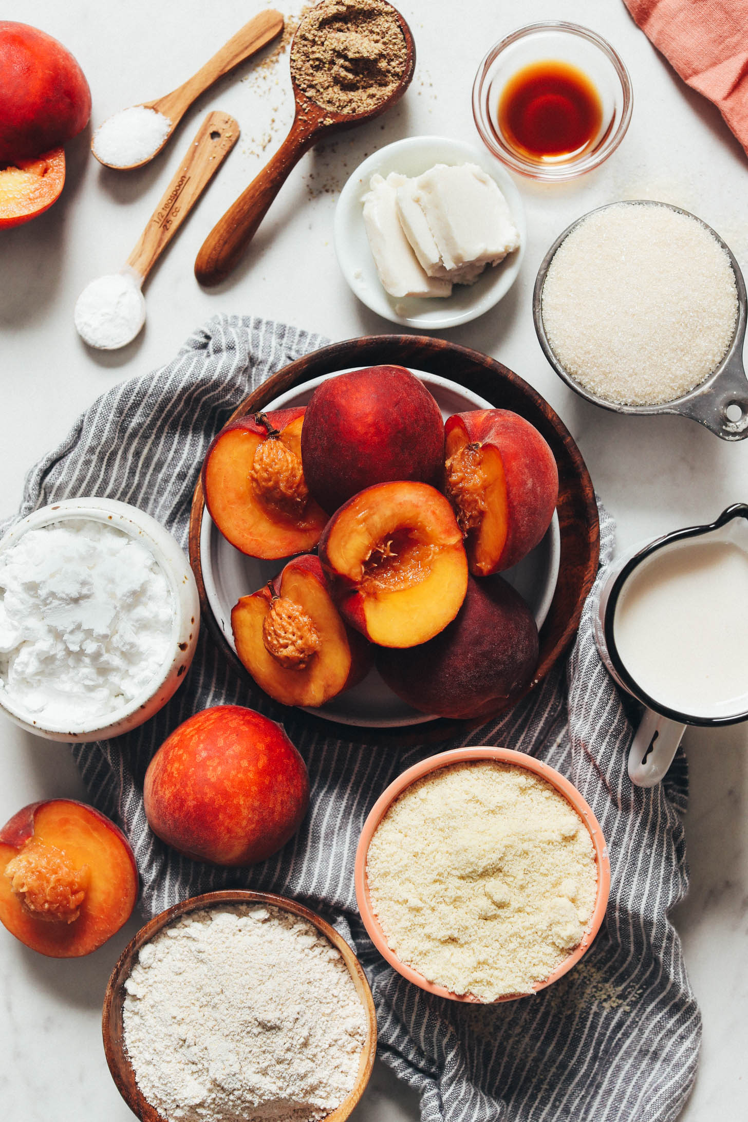 Fresh peaches surrounded by almond flour, potato starch, almond milk, sugar, vegan butter, vanilla, flaxseed meal, salt, and baking powder