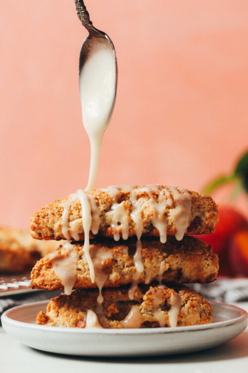 Drizzling vanilla glaze over a stack of peach scones