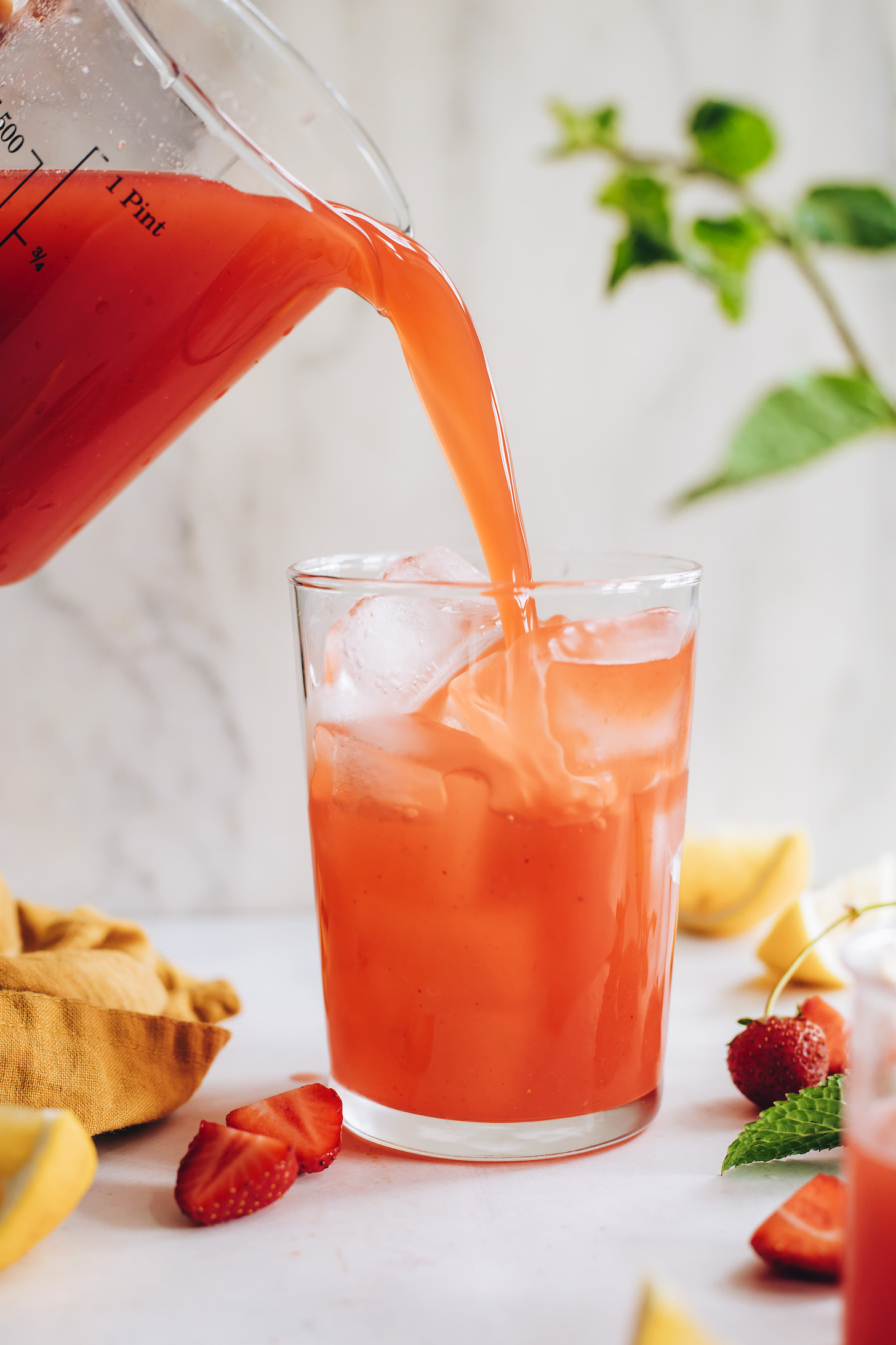 Pouring strawberry lemonade over a glass of ice