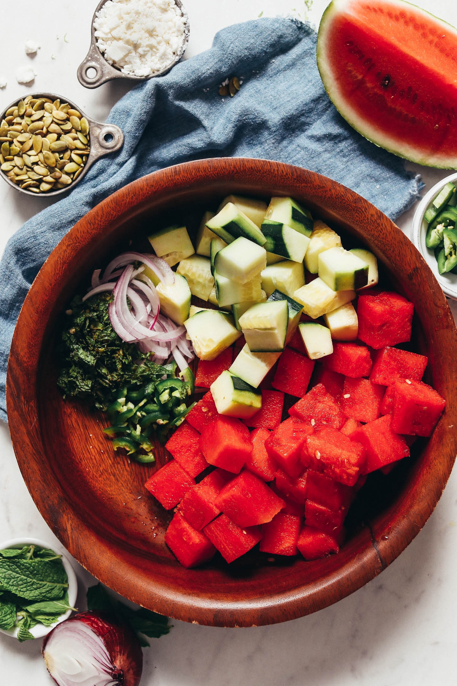 Cubed watermelon and cucumber in a bowl with sliced jalapeño, red onion, and mint