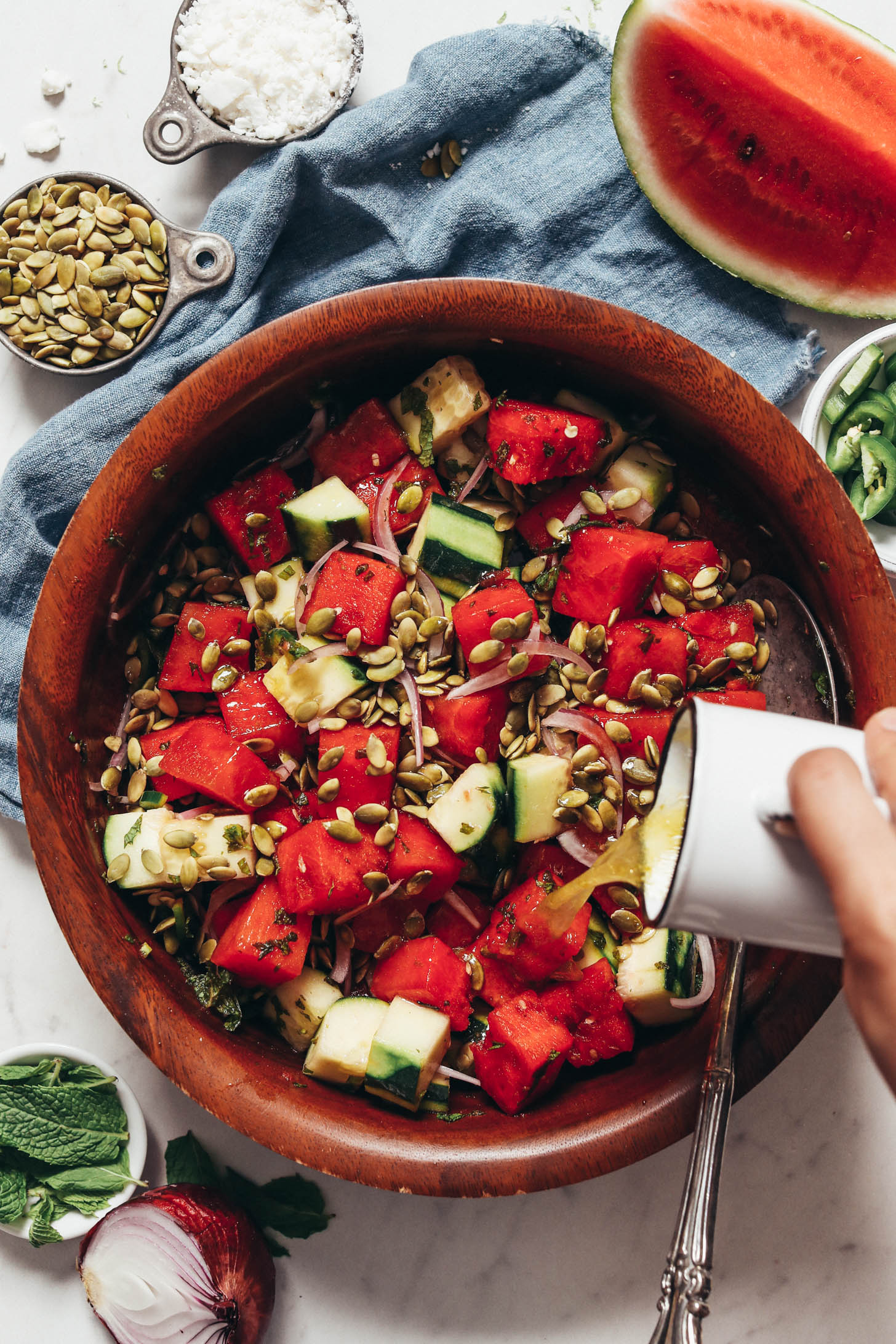 Pouring lime olive oil dressing over watermelon cucumber salad