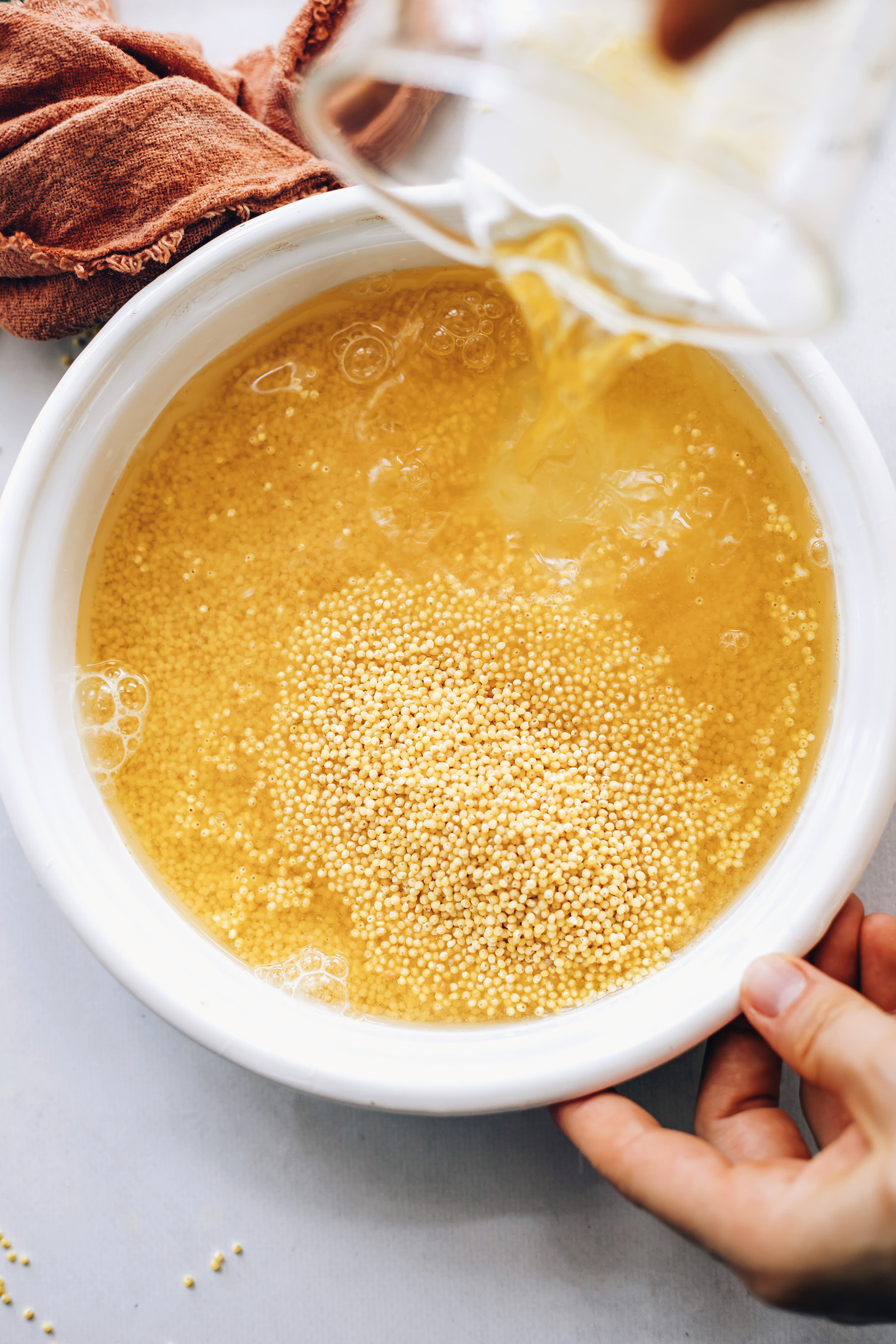 Pouring vegetable broth over dry millet in a saucepan