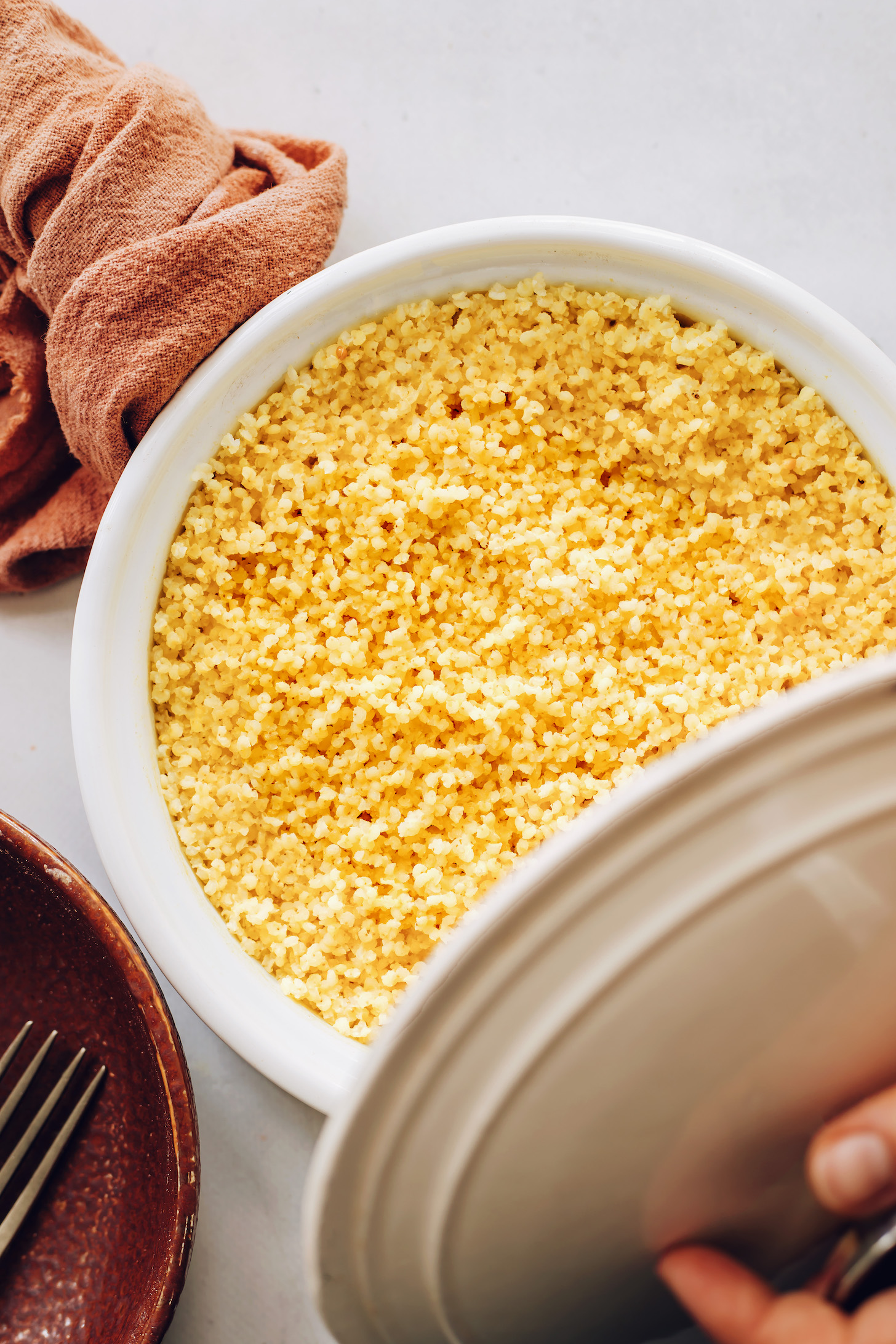 Holding a lid over a pot of cooked millet
