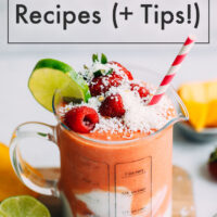 Cup of gingery mango berry smoothie topped with shredded coconut, fresh raspberries, a lime wedge, and with a paper straw