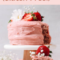 Slice of vegan and gluten-free strawberry cake with a whole strawberry cake, with fresh strawberries and flowers on top