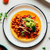 Plate with a corn tortilla topped with beans, jicama slaw, and guacamole