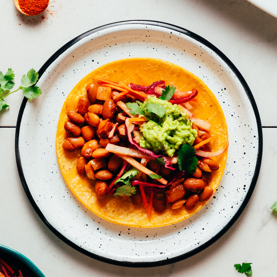 Plate with a corn tortilla topped with beans, jicama slaw, and guacamole