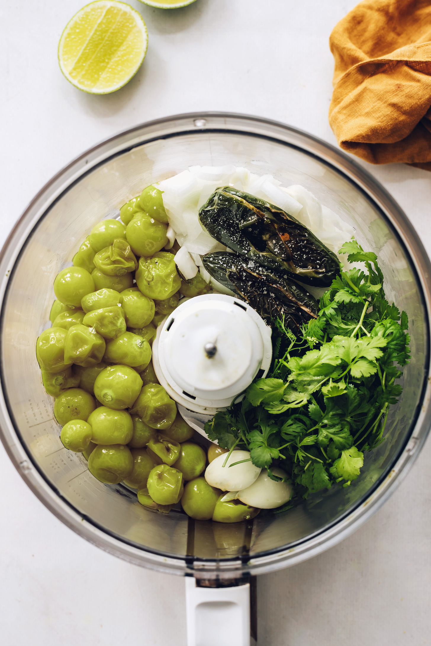 Food processor with roasted tomatillos and jalapeños, cilantro, garlic, onion, and salt