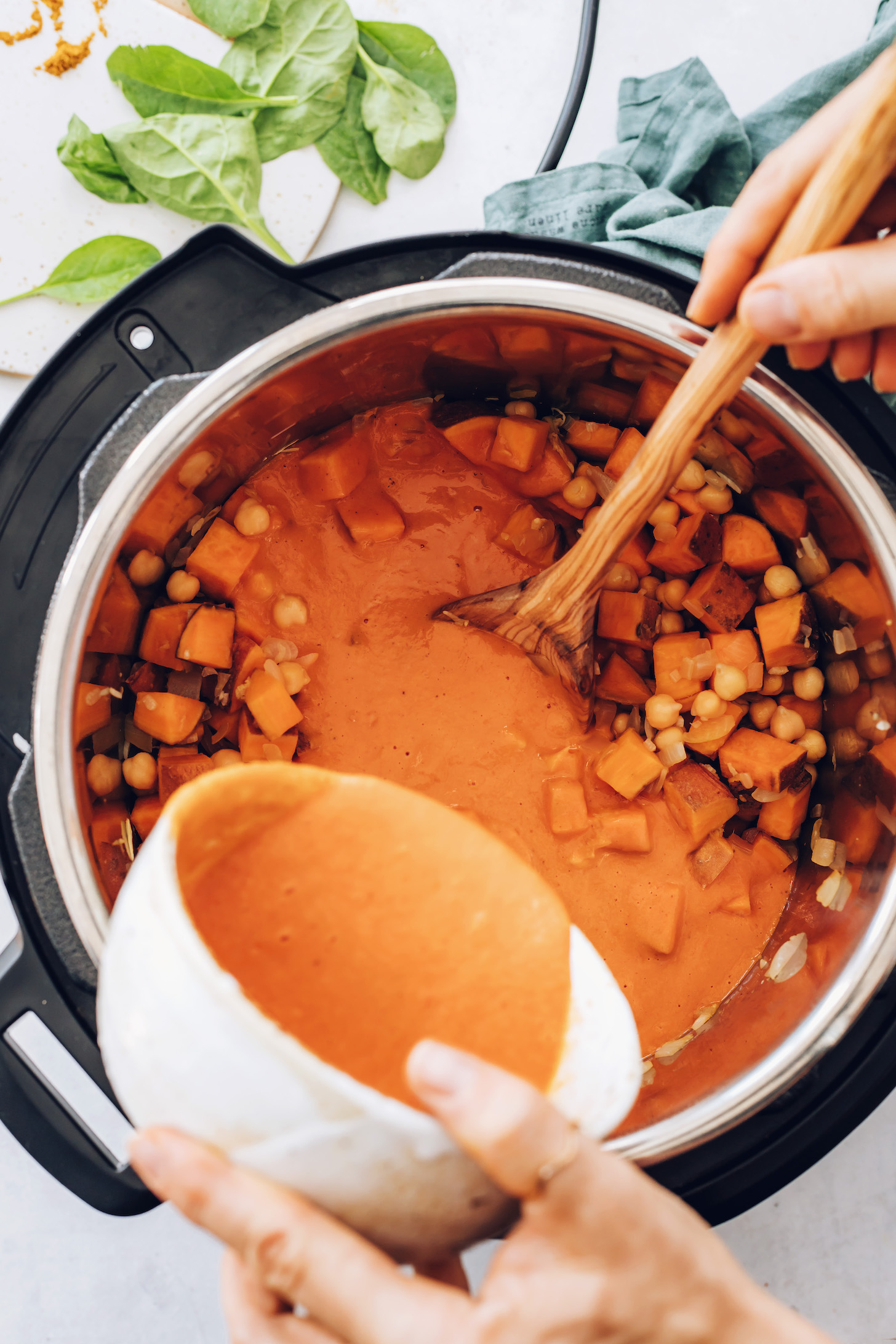 Pouring roasted red pepper sauce over sautéed onion, garlic, ginger, sweet potatoes, and chickpeas