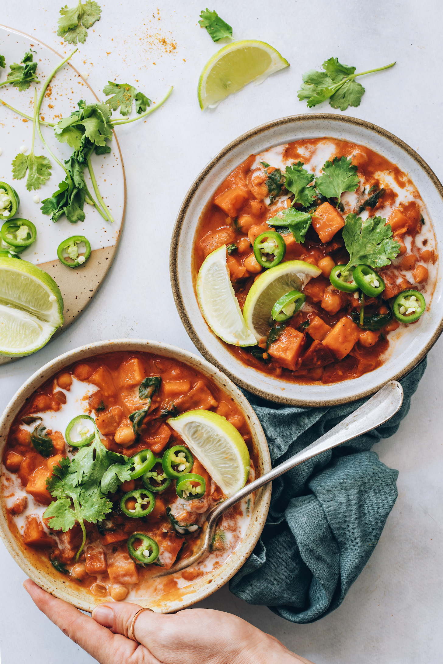 Two bowls of roasted red pepper chickpea curry topped with cilantro, lime wedges, and jalapeño