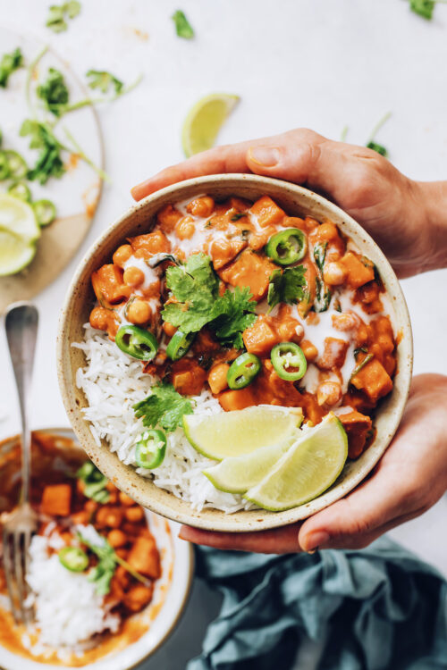 Hands holding a bowl of roasted red pepper curry with white rice