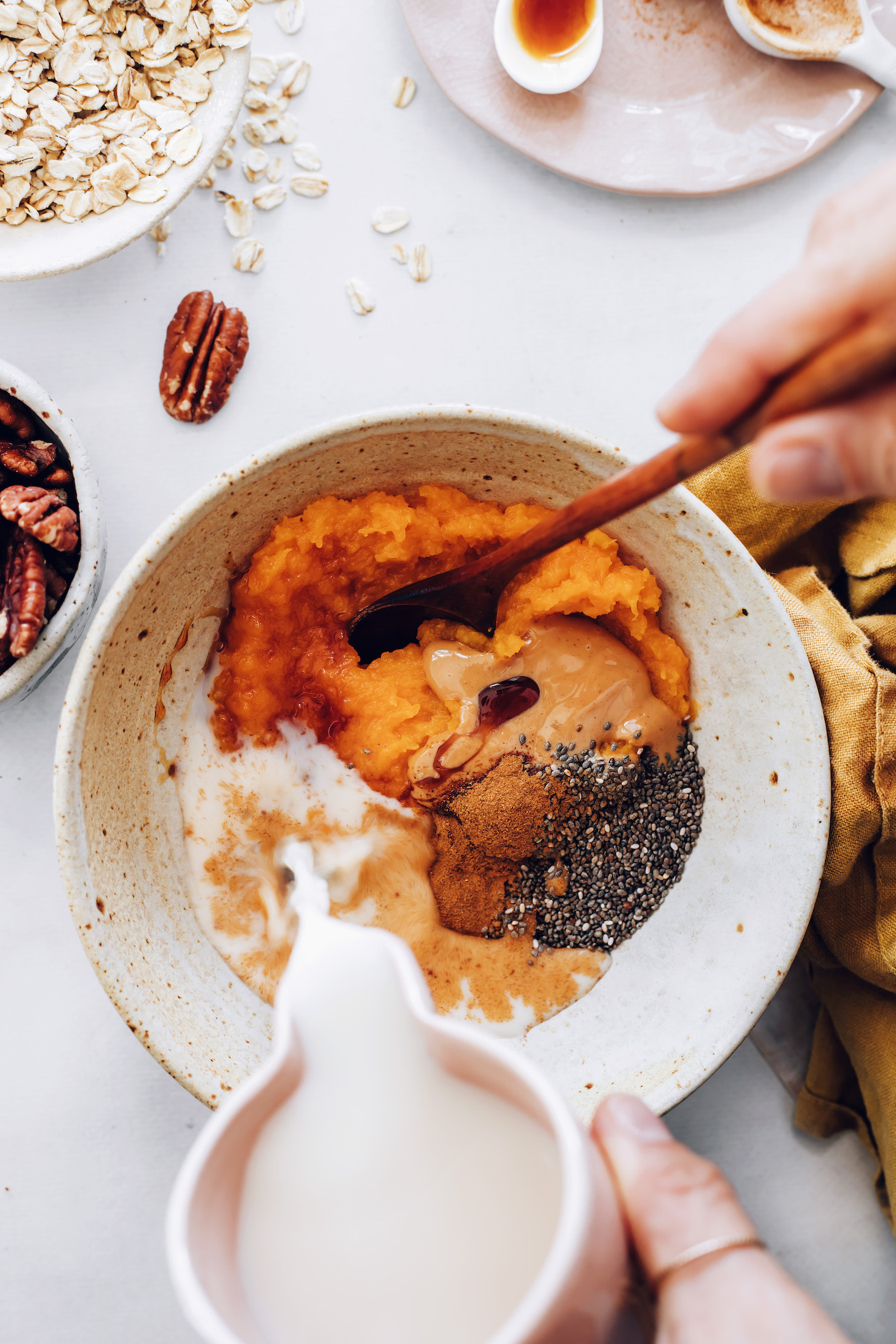 Pouring almond milk into a bowl of pumpkin purée, almond butter, pumpkin pie spice, and chia seeds