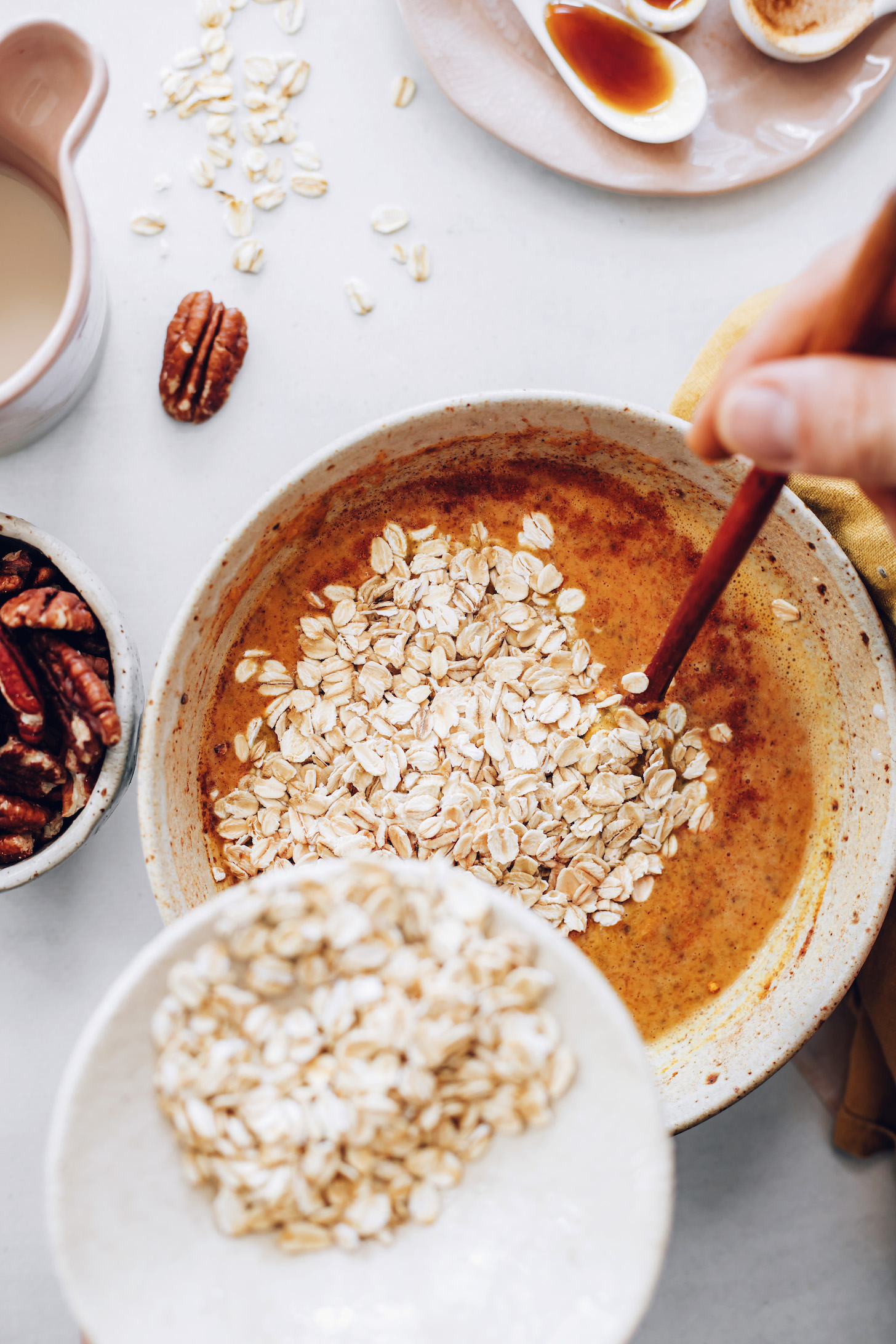 Pouring rolled oats into a bowl of pumpkin purée, almond milk, and other wet ingredients