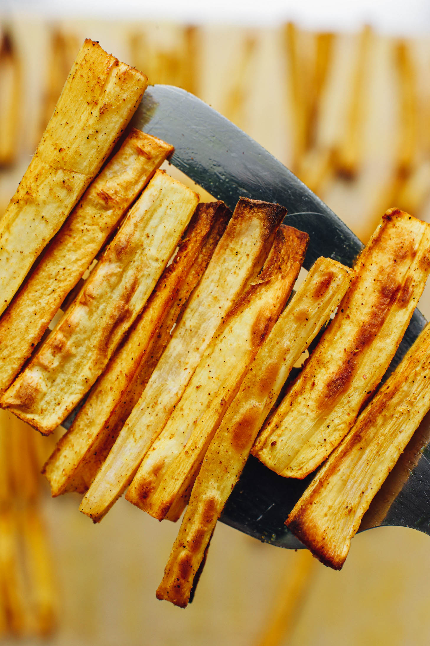 Holding up a spatula of perfectly roasted parsnip fries