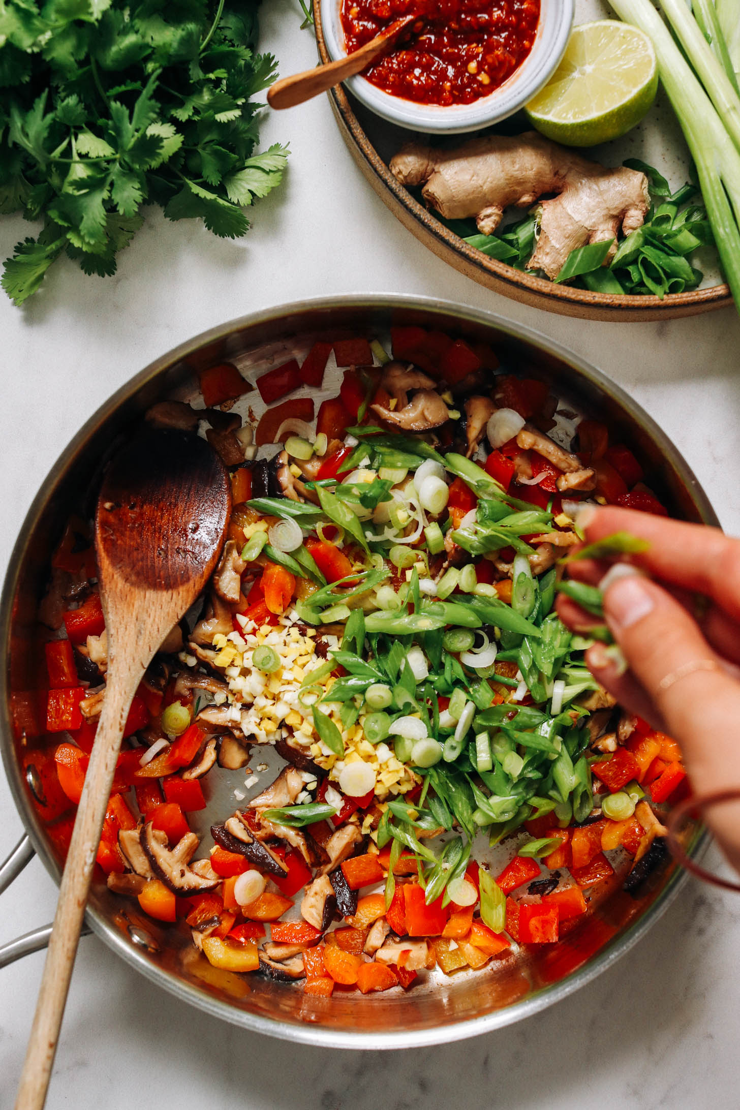 Adding sliced green onion into a skillet of sautéed veggies