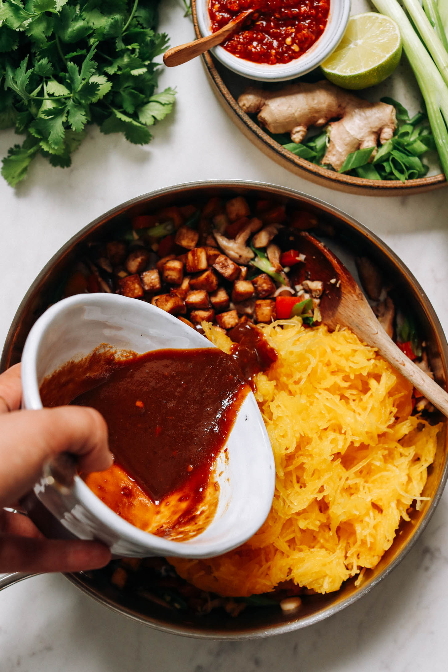 Pouring peanut sauce over spaghetti squash, tofu, and veggies