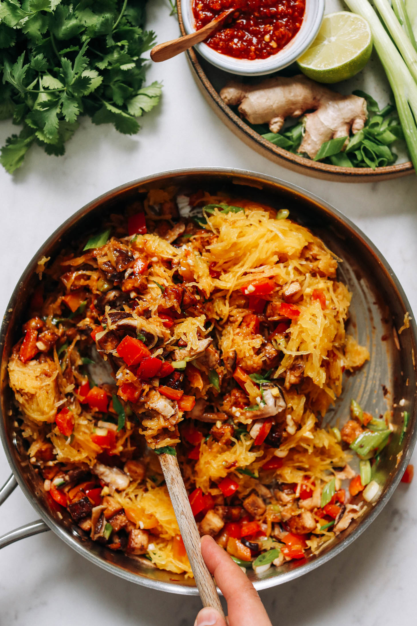 Stirring a pan of spaghetti squash stir fry with bell peppers and mushrooms