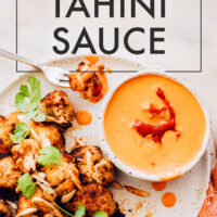 Bowl of vegan 5-minute harissa tahini sauce with roasted cauliflower on the side and roasted almonds sprinkled on top