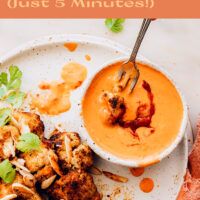 Bowl of vegan 5-minute harissa tahini sauce with roasted cauliflower on the side and roasted almonds sprinkled on top