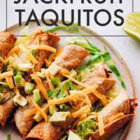 Plate of crispy vegan baked jackfruit taquitos with green onions, and vegan cheese on top