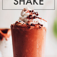 Glass of vegan jamocha shake with coconut whipped cream, chocolate and caramel drizzle, and cacao nibs on top